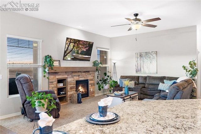 living area with ceiling fan, baseboards, light colored carpet, and a stone fireplace