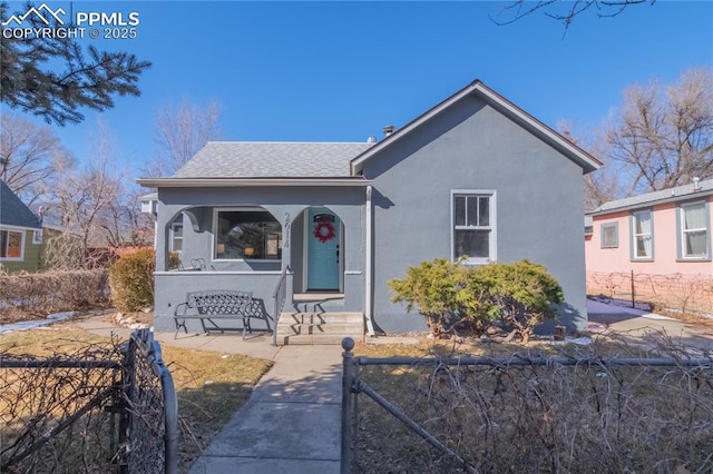 bungalow-style house with roof with shingles, fence, and stucco siding