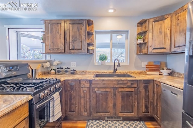 kitchen featuring open shelves, appliances with stainless steel finishes, a sink, light stone countertops, and plenty of natural light