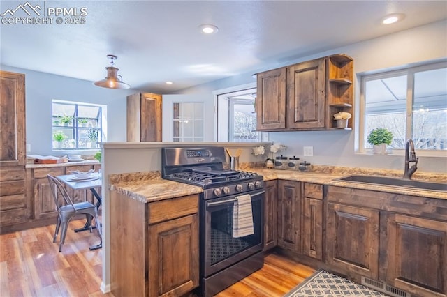 kitchen featuring stainless steel range with gas cooktop, open shelves, visible vents, light wood-style flooring, and a sink