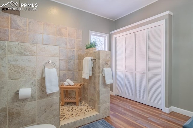 bathroom with a tile shower, wood finished floors, and baseboards