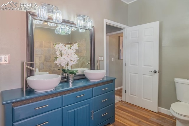 full bathroom with toilet, double vanity, a sink, and wood finished floors