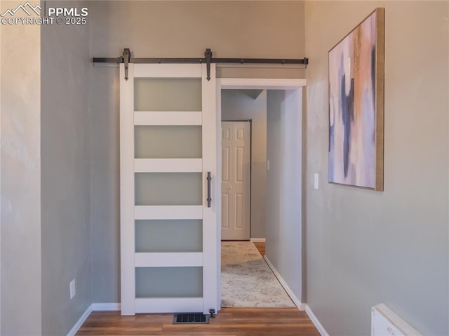 hallway with a barn door, visible vents, baseboards, and wood finished floors