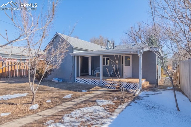 ranch-style home featuring a porch, fence, a shingled roof, and stucco siding