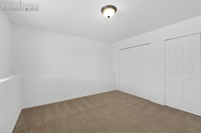 unfurnished bedroom featuring carpet flooring, baseboards, and two closets