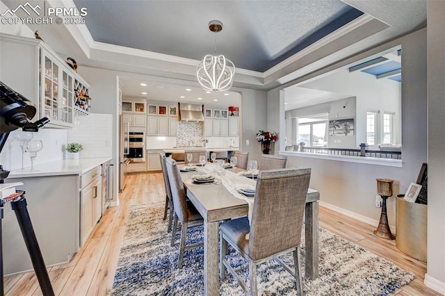 dining room with light wood-type flooring, a chandelier, a raised ceiling, and crown molding