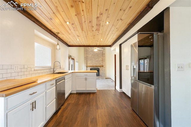 kitchen featuring a peninsula, butcher block countertops, a sink, white cabinetry, and pendant lighting