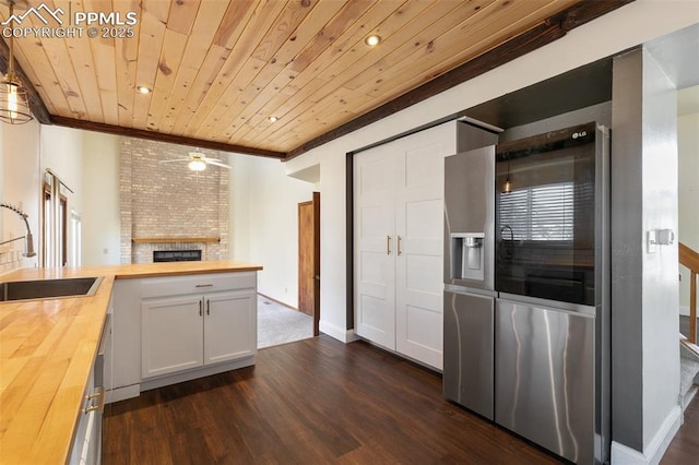 kitchen with butcher block counters, wooden ceiling, a sink, and white cabinets