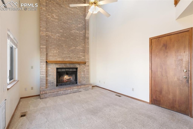 unfurnished living room featuring a brick fireplace, a towering ceiling, visible vents, and light colored carpet