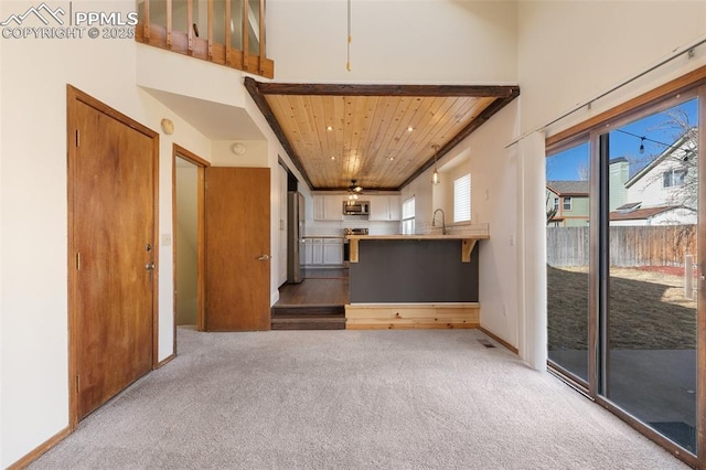 unfurnished living room featuring wooden ceiling, a sink, a towering ceiling, and light colored carpet