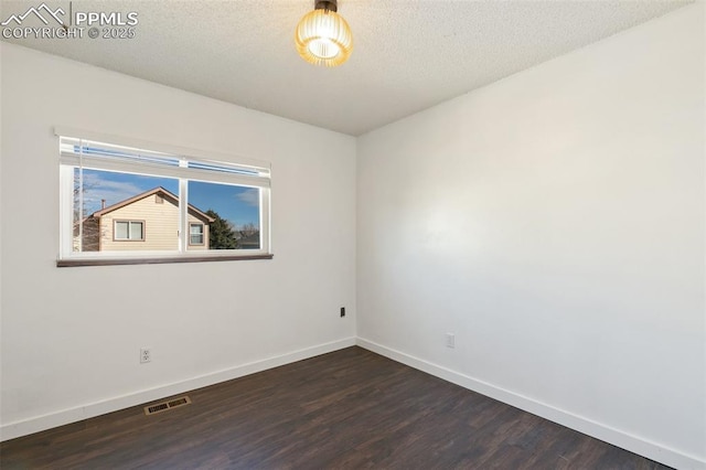 spare room with baseboards, a textured ceiling, visible vents, and dark wood-style flooring