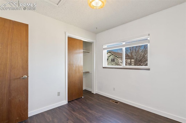 unfurnished bedroom with baseboards, visible vents, dark wood-style floors, a textured ceiling, and a closet