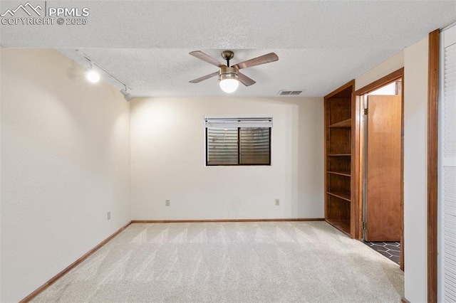 spare room with a textured ceiling, light colored carpet, visible vents, baseboards, and track lighting