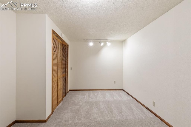 interior space featuring a closet, light colored carpet, baseboards, and track lighting