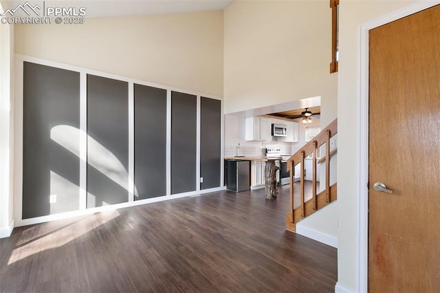 foyer featuring a high ceiling, dark wood-style flooring, a ceiling fan, baseboards, and stairs