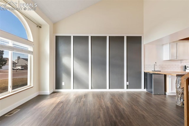 interior space with baseboards, visible vents, dark wood-style floors, high vaulted ceiling, and a sink