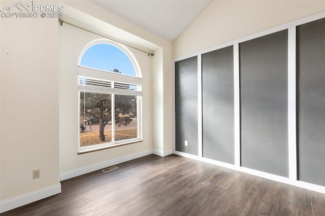 interior space with baseboards, visible vents, vaulted ceiling, and dark wood-type flooring