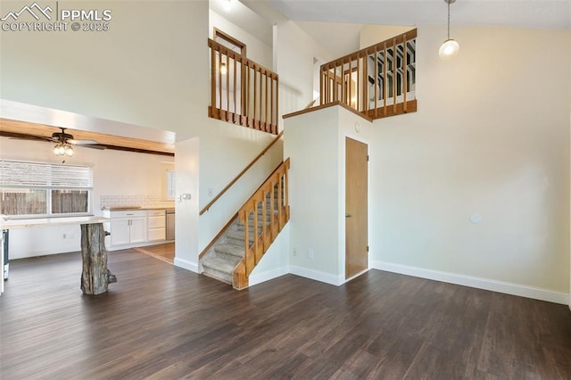 unfurnished living room with ceiling fan, dark wood-style flooring, a towering ceiling, baseboards, and stairway