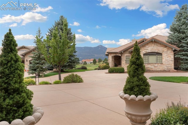 view of front of home featuring stone siding, curved driveway, a mountain view, and a tiled roof