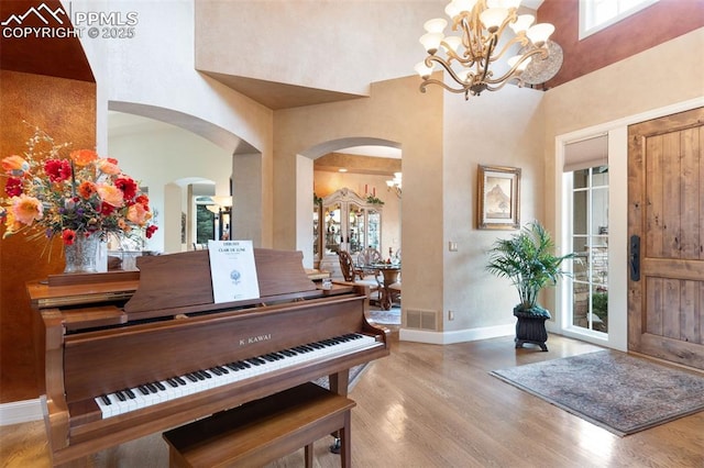 entryway with a towering ceiling, an inviting chandelier, baseboards, and wood finished floors