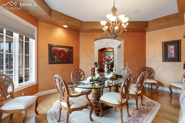 dining space with arched walkways, baseboards, an inviting chandelier, and wood finished floors