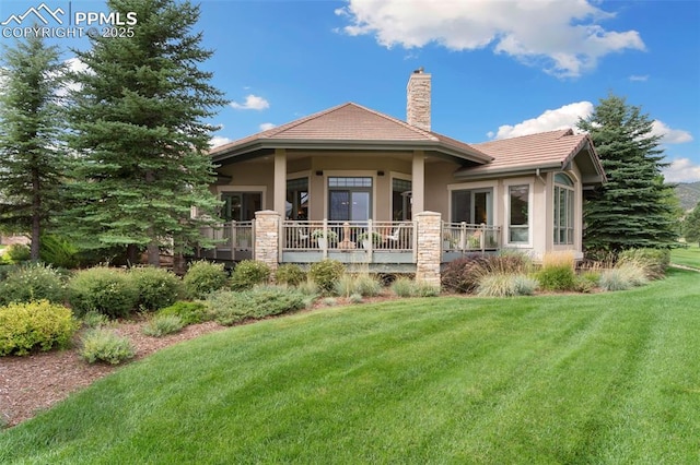 rear view of property featuring a tile roof, a lawn, a chimney, and stucco siding