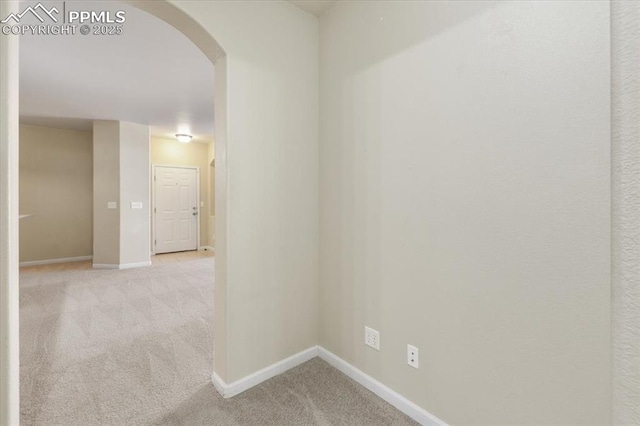 corridor with arched walkways, light carpet, and baseboards