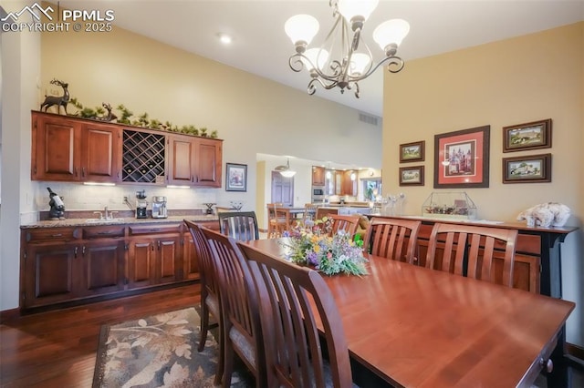 dining room with a chandelier, lofted ceiling, visible vents, wet bar, and dark wood finished floors