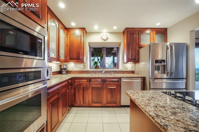 kitchen featuring stainless steel appliances, recessed lighting, glass insert cabinets, a sink, and light stone countertops