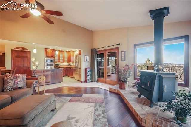 living area with french doors, light wood finished floors, a ceiling fan, a wood stove, and high vaulted ceiling