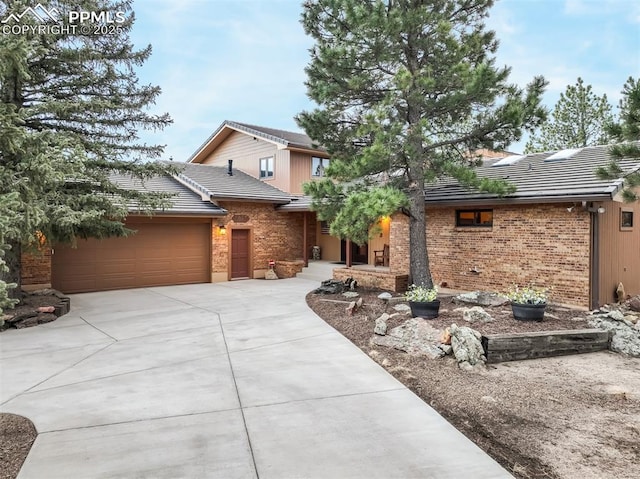 view of front of home with an attached garage, a tiled roof, brick siding, and concrete driveway