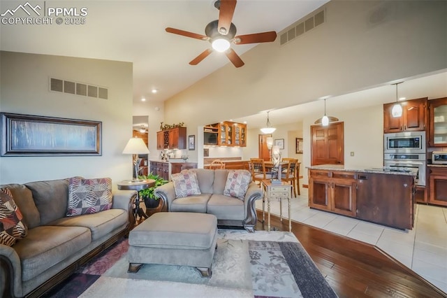 living area featuring light wood-style flooring, visible vents, vaulted ceiling, and a ceiling fan