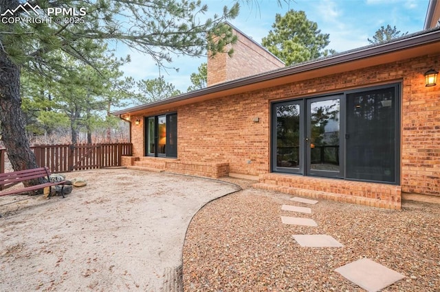 rear view of property with entry steps, a chimney, fence, a patio area, and brick siding