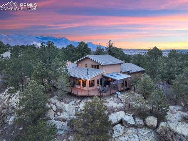 back of house at dusk featuring a deck with mountain view and a tile roof