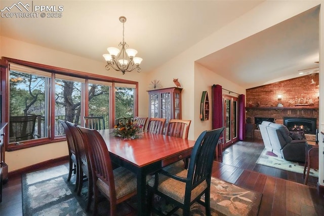 dining space featuring baseboards, dark wood finished floors, vaulted ceiling, a brick fireplace, and a chandelier