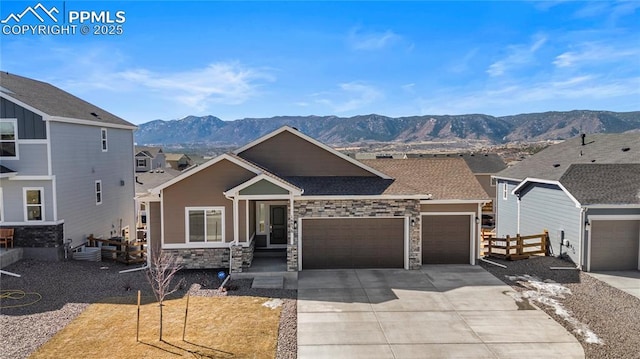 view of front of house with driveway, stone siding, fence, a mountain view, and a garage