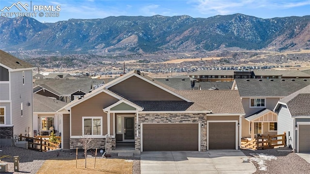 view of front of home with a garage, concrete driveway, stone siding, roof with shingles, and a mountain view