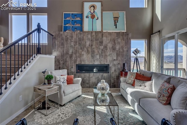 living area with stairway, a tiled fireplace, a towering ceiling, and baseboards