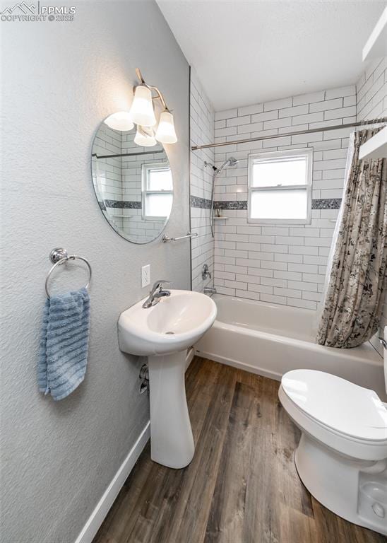 full bath with shower / bath combo, baseboards, a textured wall, toilet, and wood finished floors