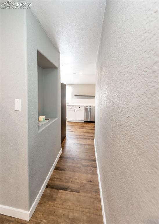 corridor featuring a textured ceiling, baseboards, wood finished floors, and a textured wall