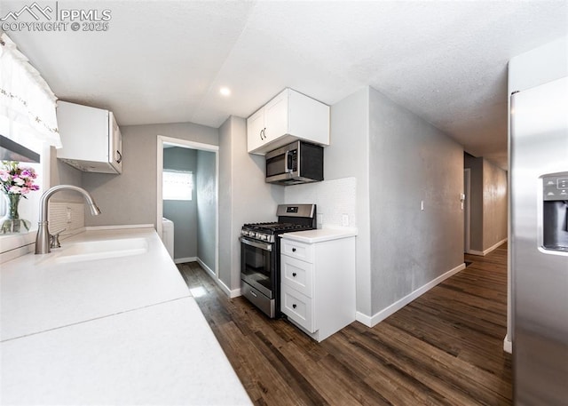 kitchen with white cabinets, appliances with stainless steel finishes, dark wood-type flooring, light countertops, and a sink