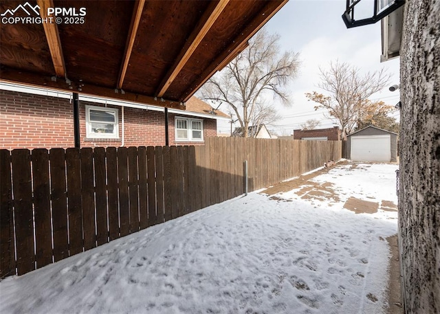 snowy yard with an outdoor structure, fence, and a detached garage