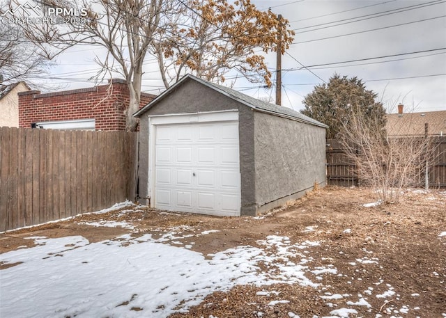 snow covered garage featuring a garage and fence