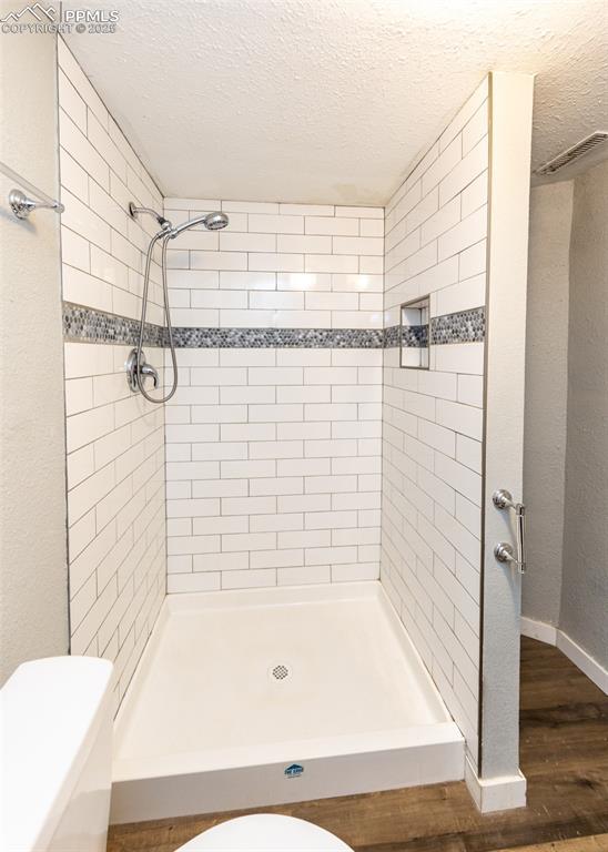 bathroom with a textured ceiling, a stall shower, wood finished floors, and toilet