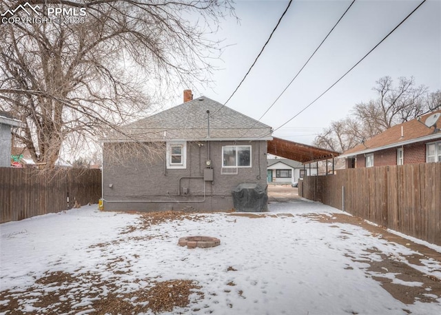 snow covered house with a chimney, fence, and a fire pit