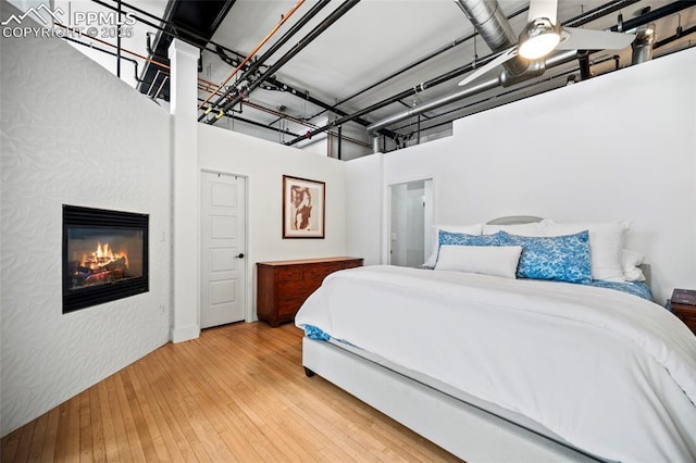 bedroom featuring a ceiling fan, hardwood / wood-style floors, and a glass covered fireplace