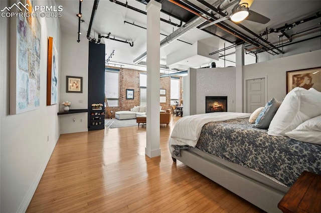 bedroom featuring a fireplace, baseboards, track lighting, and wood finished floors