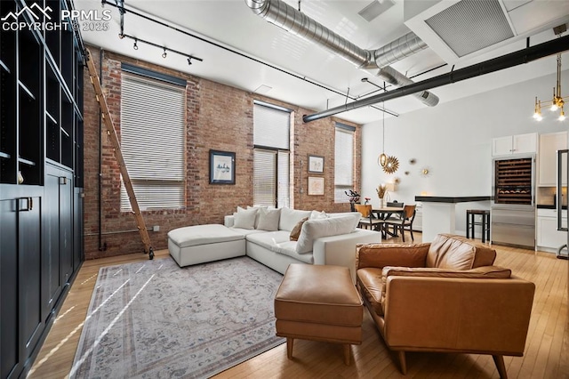 living area featuring light wood-style floors, rail lighting, a high ceiling, and brick wall