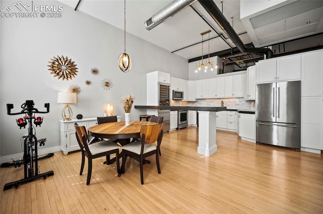 dining area featuring baseboards, light wood-style flooring, and a high ceiling