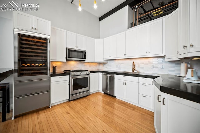 kitchen with tasteful backsplash, dark countertops, a towering ceiling, appliances with stainless steel finishes, and a sink